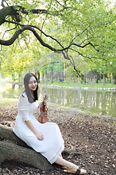 Portrait of Aisan Chinese girl woman play violin in nature park garden under a tree enjoy leisure time performance outdoor in park