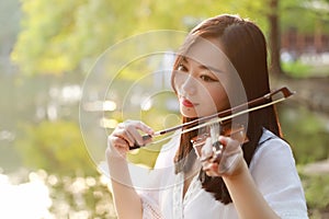 Portrait of Aisan Chinese girl woman play violin in nature park by lake sunset enjoy leisure time performance outdoor in park