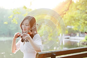 Portrait of Aisan Chinese girl woman play violin in nature park by lake sunset enjoy leisure time performance outdoor in park