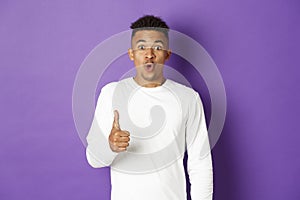 Portrait of amazed african-american man, showing thumbs-up and looking excited, recommend and praise good product