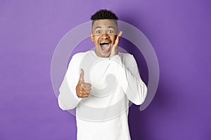 Portrait of amazed african-american man, showing thumbs-up and looking excited, recommend and praise good product