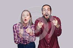 Portrait of amazed bearded man and woman in casual style standing, pointing and looking at camera with surprised unbelievable