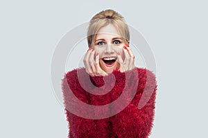 Portrait of amazed beautiful young blond woman in red blouse standing and looking at camera with surprised face and happiness news
