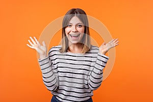 Portrait of amazed beautiful young woman with brown hair in long sleeve striped shirt. indoor studio shot isolated on orange