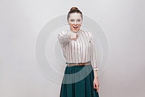 Portrait of amazed beautiful young woman in striped shirt and green skirt with makeup and collected ban hairstyle, standing