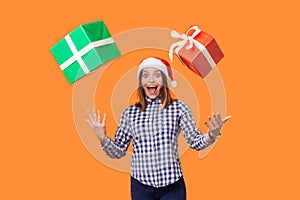Portrait of amazed brunette woman in santa hat and checkered shirt standing with open mouth and raised hands, trying to catch