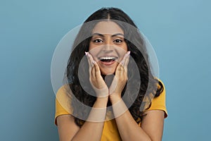 Portrait of amazed young indian woman touching her face