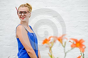 Portrait of amazed young woman in glasses with orange flowers standing over white brick background