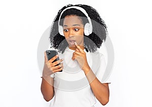 Portrait of amazed young woman in headphones looking at phone