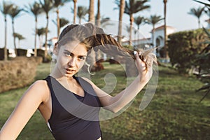 Portrait amazing attractive young woman in sportswear playing with her long curly hair in park of tropical city. Looking photo