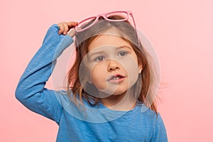 Portrait of amazing beautiful adorable little girl taking off glamour pink glasses and looking with dreamy expression