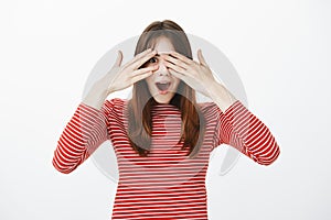 Portrait of amazing european girl in casual clothes, covering eyes and peeking through fingers being surprised and happy