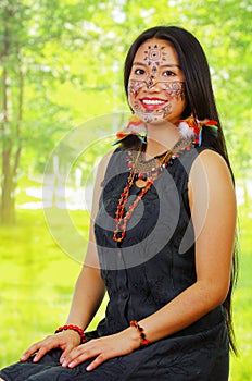 Portrait amazonian exotic woman with facial paint and black dress, posing proudly for camera, forest background.