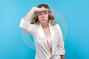 Portrait of ambitious businesswoman keeping curious look far away with hand over eye. blue background