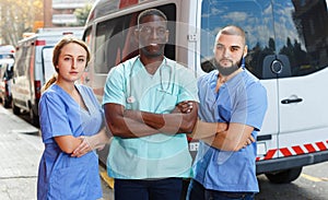 Portrait of ambulance team of three standing near ambulance car