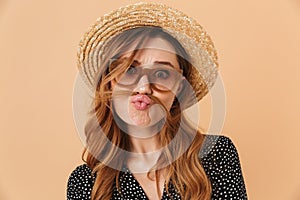 Portrait of amusing funny woman 20s wearing straw hat and sunglasses fooling around and putting hair like mustache, isolated over