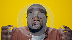 Portrait of angry african man screaming in sunglasses on yellow background.