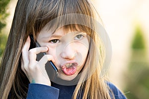 Portrait of angry child girl with long hair talking on cell phone. Little female kid having discussion on smartphone. Children