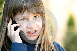 Portrait of angry child girl with long hair talking on cell phone. Little female kid having discussion on smartphone. Children