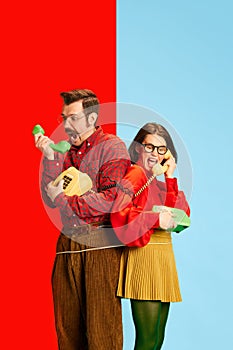 Portrait with angry couple man and beautiful woman holding telephone receivers and screaming over blue background. Toxic