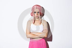 Portrait of angry cute girl with pink wig and glamour makeup, cross arms on chest and sulking mad at someone, feeling