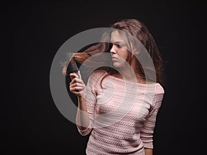 Woman brushing tangled hair with a comb on a black background. Girl looking at damaged sick hair. Hair problems concept.