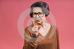 Portrait of angry grey haired old strict senior woman wearing glasses pointing up threatening with finger. Grandmother isolated