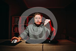 Portrait of an angry guy gamer playing video games at night on the computer, looking with a scary face at the screen and showing a