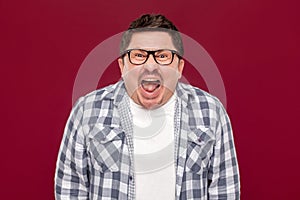 Portrait of angry handsome middle aged business man in casual checkered shirt and eyeglasses standing, looking and screaming at