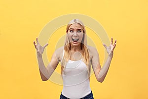 Portrait of an angry irritated woman with hands raised shouting at camera on yellow background