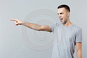 Portrait of angry irritated young man in casual clothes swearing pointing index finger aside isolated on grey wall