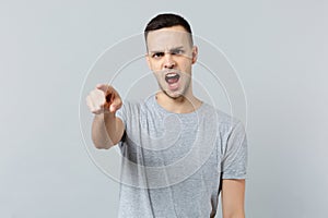 Portrait of angry irritated young man in casual clothes swearing, pointing index finger on camera isolated on grey