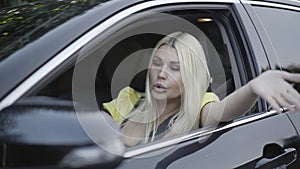 Portrait of angry irritated young woman sitting on driver`s seat in car and talking. Annoyed beautiful blond Caucasian