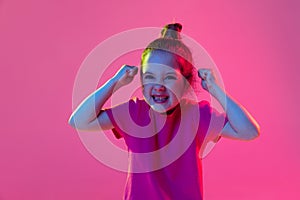 Portrait of angry little girl, kid wearing pink t-shirt posing isolated on magenta color background. Concept of children