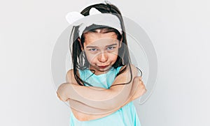 Portrait of the angry little girl wearing blue dress and white bow with crossed arms posing over white background. Displeased