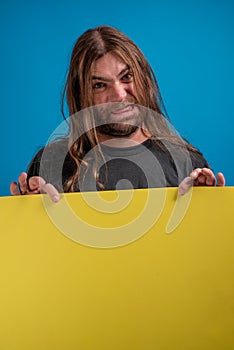 Portrait of angry male displaying a grimace while holding a yellow banner for advertise