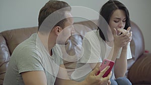 Portrait of angry man shouting at his wife showing her cellphone with messages from her paramour at home. Problems in