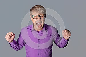 Portrait of a angry man with glasses staring at camera, shows finger and shouting over gray background
