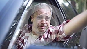 Portrait of angry man talking and gesturing out of side window sitting on driver's seat in car. Close-up of dissatisfied
