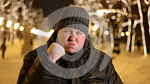 Portrait of angry man threatening by shaking his fist outdoors during cold winter evening