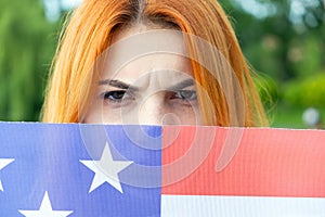 Portrait of angry red haired girl hiding her face behind USA national flag