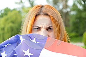 Portrait of angry red haired girl hiding her face behind USA national flag