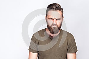 Portrait of angry sad bearded man with dark green t shirt against light gray background.