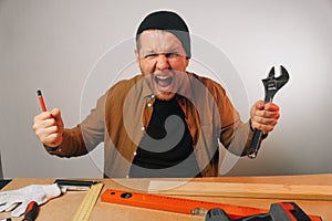 Portrait of an angry scream of a screaming male locksmith holding an adjustable wrench