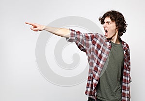 Portrait of angry screaming young man in casual clothes swearing, looking pointing index finger aside isolated on white