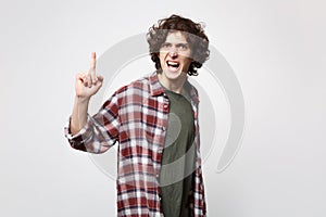Portrait of angry screaming young man in casual clothes swearing, pointing index finger up isolated on white wall