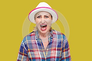 Portrait of angry or shocked modern stylish mature woman in casual style with white hat standing and looking at camera and