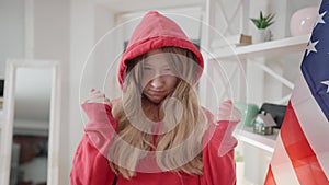 Portrait of angry teenage Asian girl putting on hood and gesturing. Furious unhappy teenager posing indoors at home with