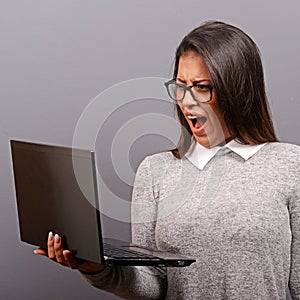 Portrait of angry woman screaming at  her laptop against gray background