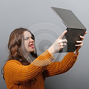 Portrait of angry woman screaming at  her laptop against gray background